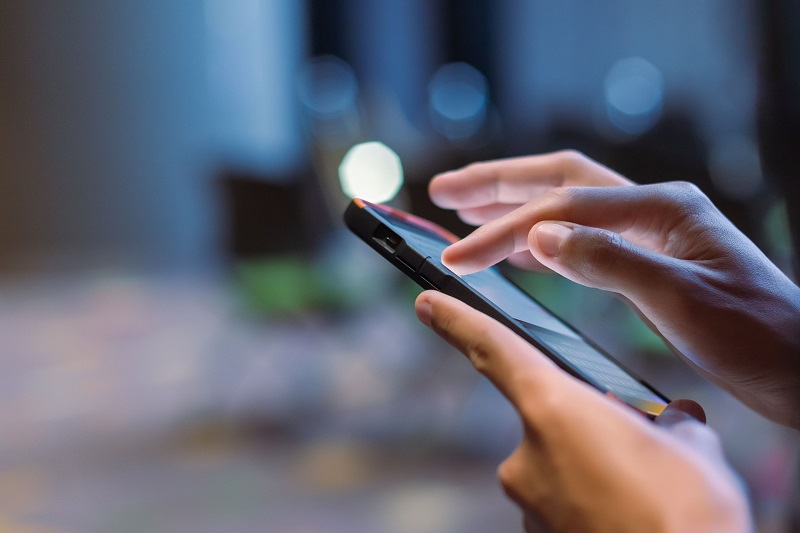 Kobieta trzyma w dłoniach smartfon i ustala limity transmisji danych, by nie dopłacać do rachunku za internet mobilny.